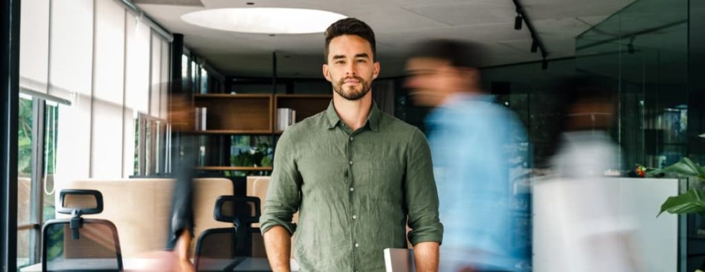 モダンなオフィスの中央で、ノートPCを手に凛とした表情で立つ40代の男性エンジニア。