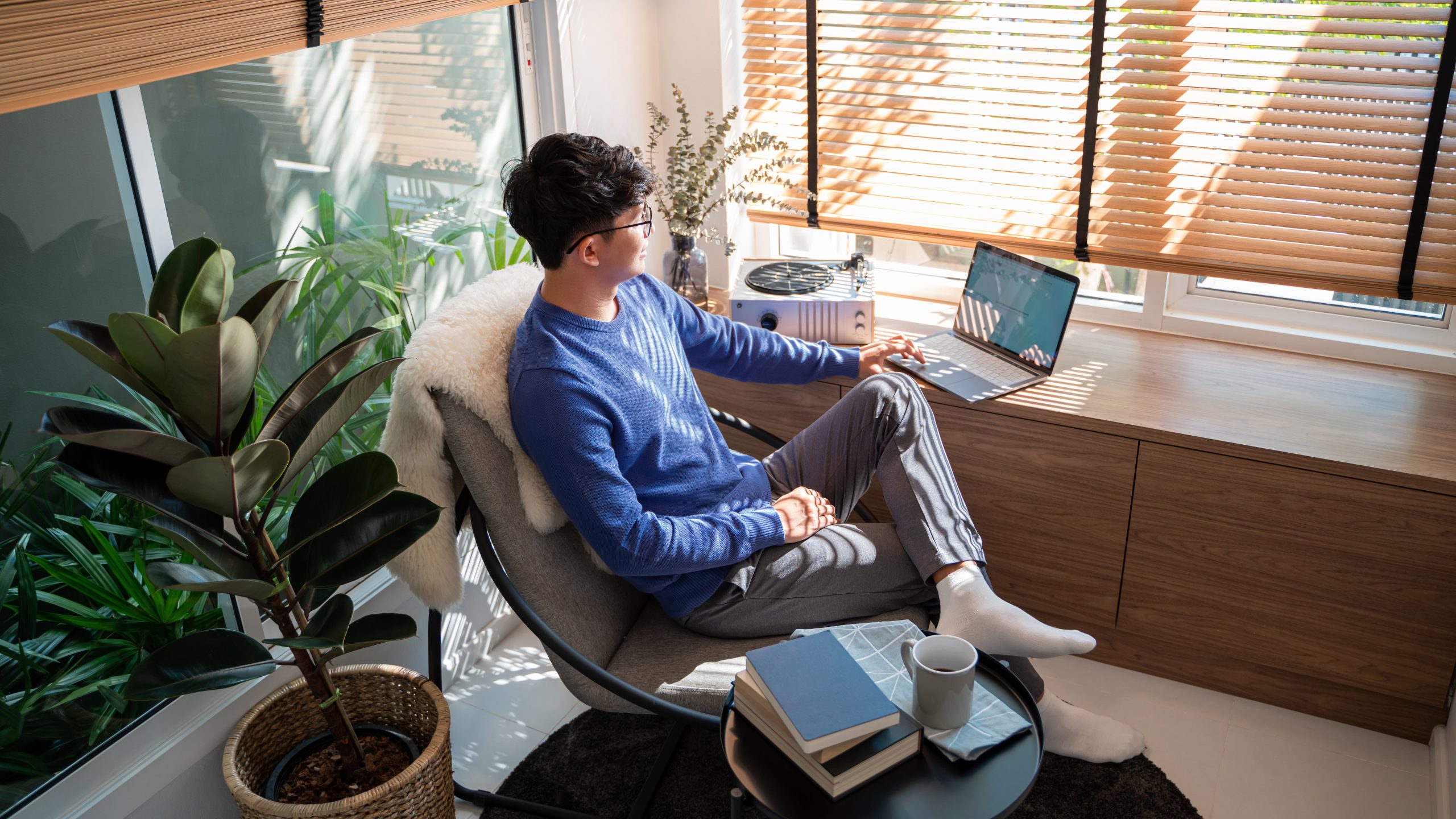 大きな窓から光が差し込む部屋で、コーヒーを片手にリモートワークを楽しむフリーランスエンジニアの男性。