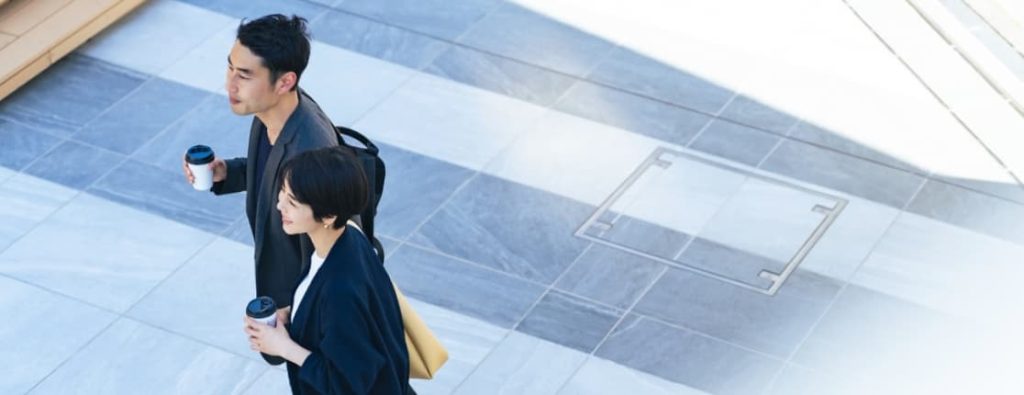 コーヒーを手に、新たなキャリアのステップへと軽やかに踏み出すビジネスパーソンの男女。
